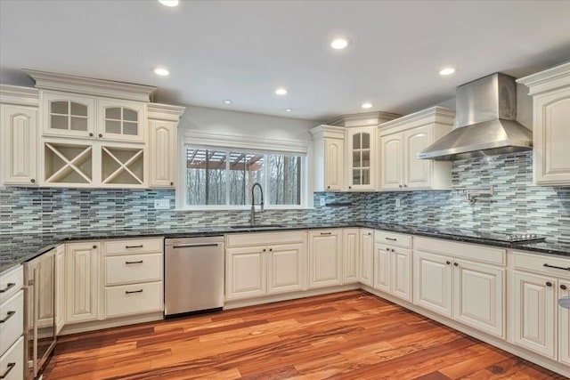 kitchen featuring stainless steel dishwasher, wall chimney exhaust hood, light wood-style flooring, stovetop, and a sink