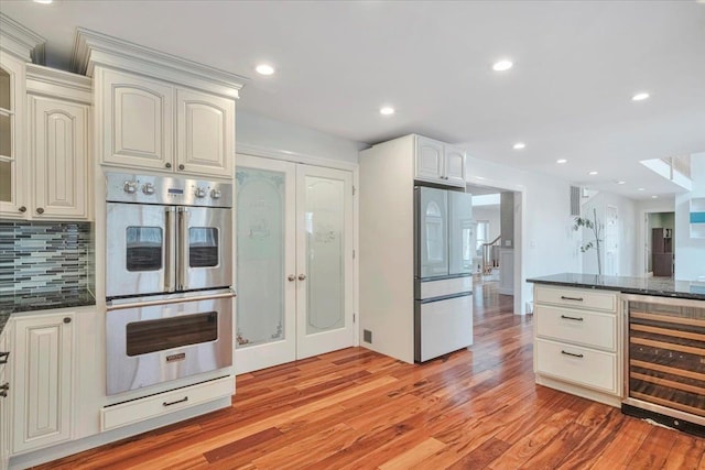 kitchen featuring recessed lighting, beverage cooler, stainless steel appliances, light wood finished floors, and backsplash