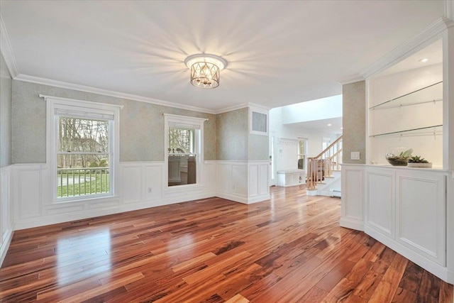 unfurnished living room featuring a wainscoted wall, a notable chandelier, hardwood / wood-style flooring, and stairs