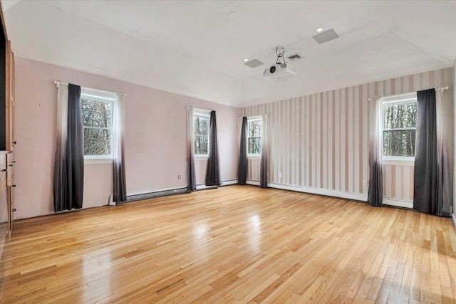 spare room featuring light wood-style flooring, a healthy amount of sunlight, visible vents, and vaulted ceiling