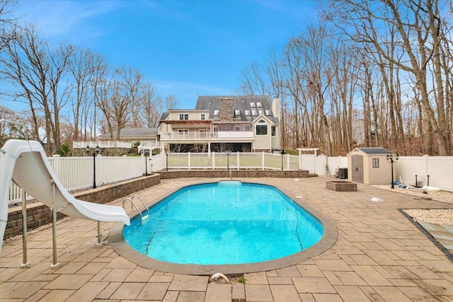 view of pool featuring a shed, a fenced backyard, a water slide, an outdoor structure, and a patio area
