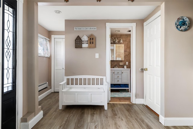 bedroom featuring ensuite bath, a baseboard heating unit, light wood-type flooring, and a closet