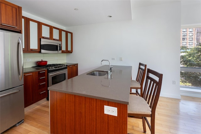 kitchen with sink, tasteful backsplash, a center island with sink, light hardwood / wood-style flooring, and appliances with stainless steel finishes