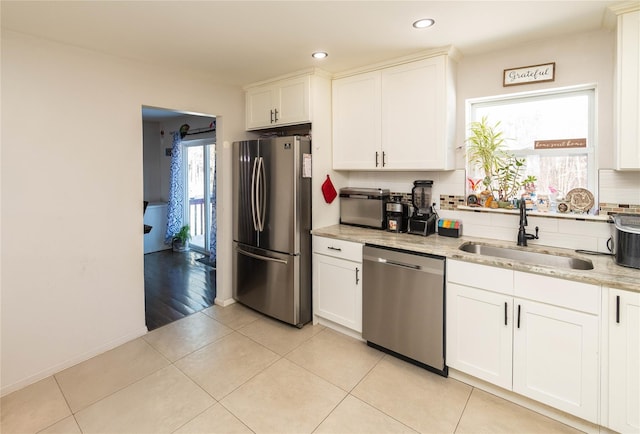 kitchen featuring sink, white cabinets, light tile patterned floors, stainless steel appliances, and light stone countertops