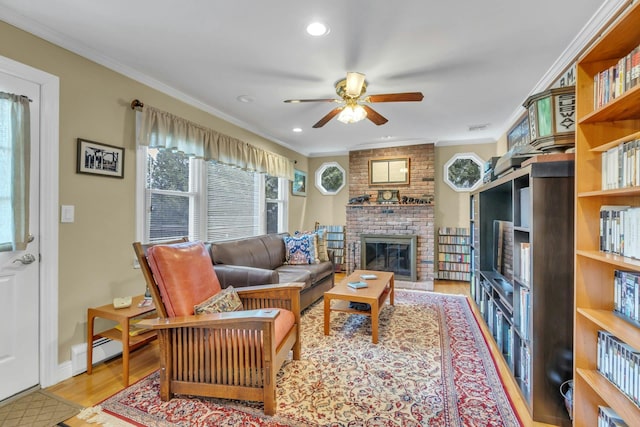 living room featuring crown molding, ceiling fan, a fireplace, and light wood-type flooring