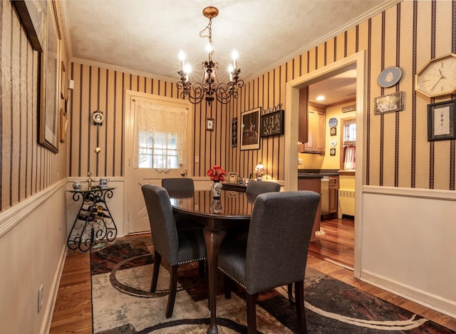 dining space featuring hardwood / wood-style floors, a notable chandelier, radiator heating unit, and ornamental molding