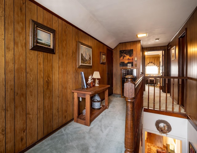 hall with lofted ceiling, wooden walls, and light colored carpet