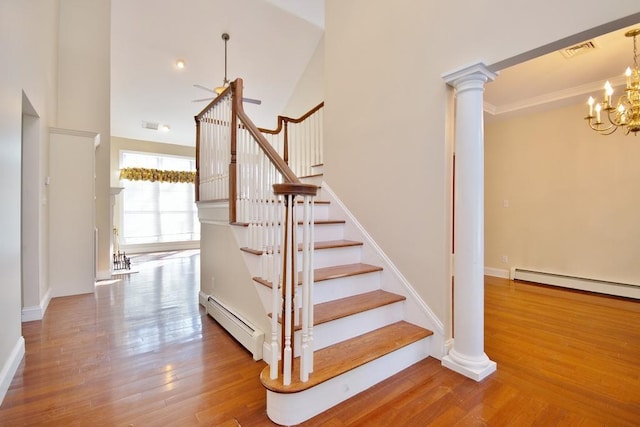 stairway with visible vents, a baseboard heating unit, wood finished floors, a chandelier, and ornate columns