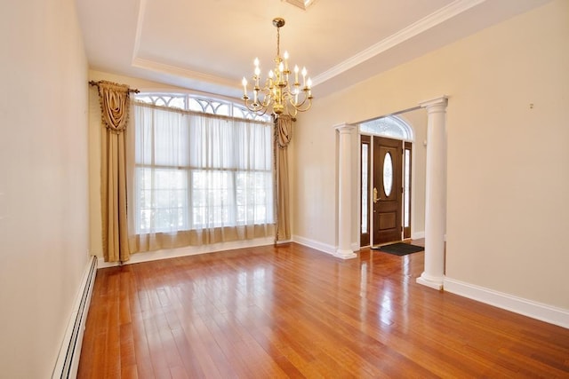 empty room featuring wood finished floors, baseboards, baseboard heating, a tray ceiling, and decorative columns