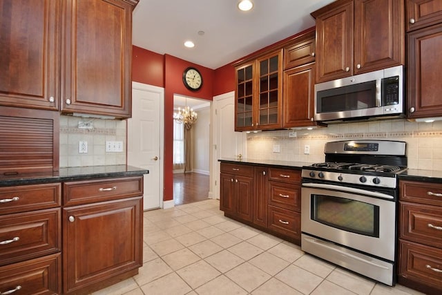 kitchen featuring light tile patterned flooring, baseboards, appliances with stainless steel finishes, dark stone counters, and glass insert cabinets