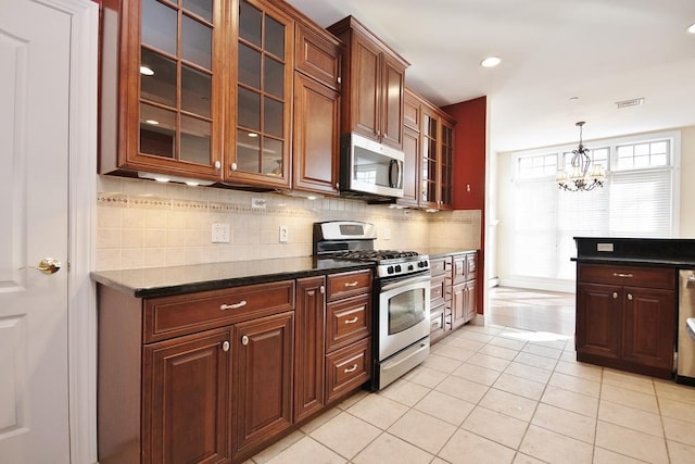 kitchen with visible vents, glass insert cabinets, appliances with stainless steel finishes, dark stone countertops, and backsplash