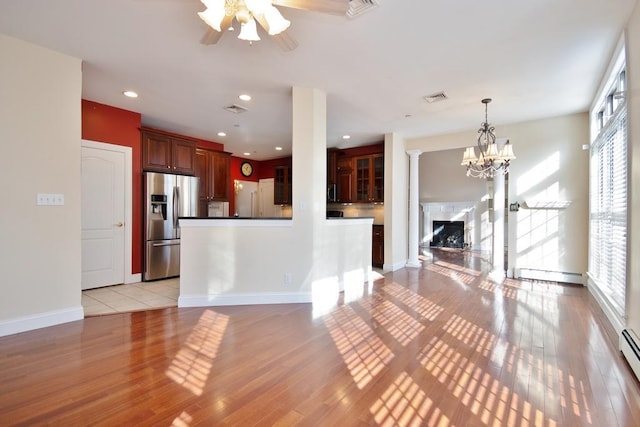 unfurnished living room with visible vents, baseboard heating, light wood-style floors, a fireplace, and a baseboard heating unit