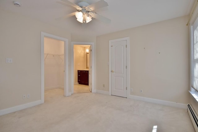 unfurnished bedroom featuring a closet, a spacious closet, a baseboard heating unit, light carpet, and baseboards