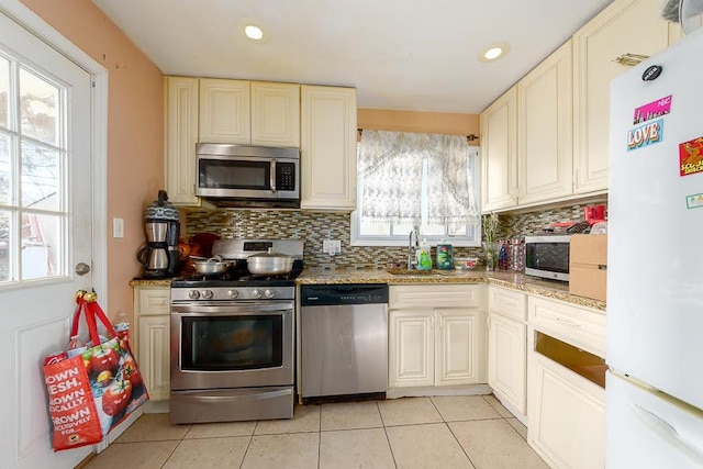 kitchen with light stone counters, appliances with stainless steel finishes, light tile patterned flooring, and sink