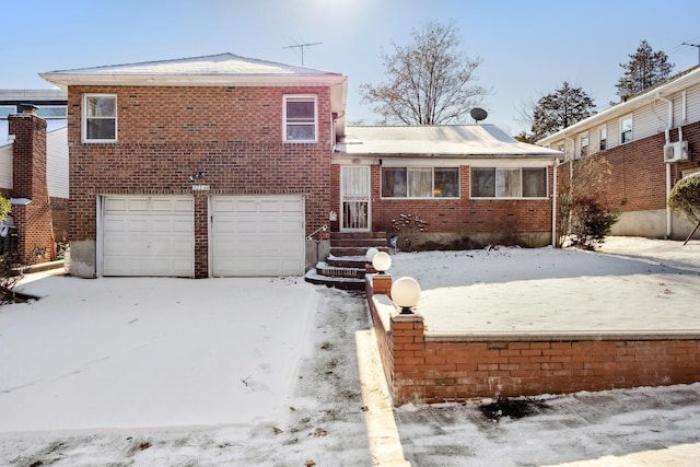 snow covered property featuring a garage and an AC wall unit