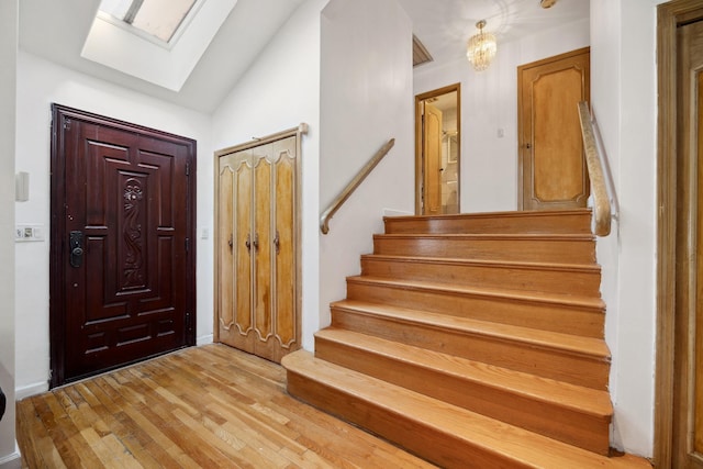 foyer entrance featuring lofted ceiling with skylight and light hardwood / wood-style floors