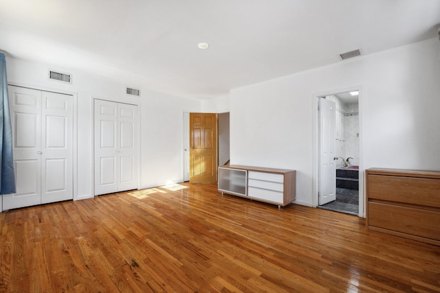 unfurnished bedroom featuring hardwood / wood-style floors, ensuite bathroom, and two closets