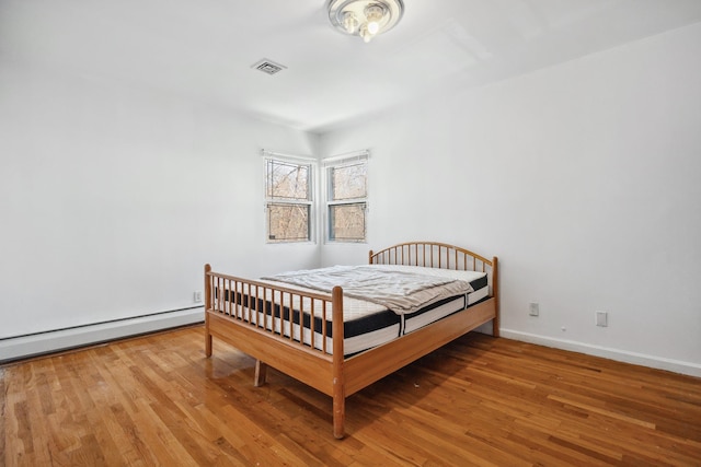 bedroom featuring a baseboard heating unit and hardwood / wood-style floors