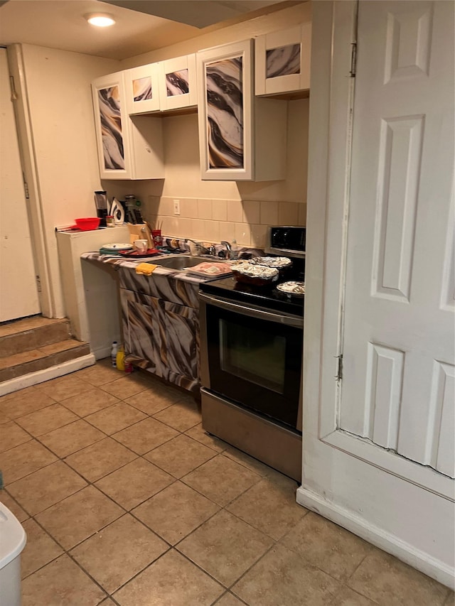 kitchen with stainless steel range with electric stovetop, light tile patterned floors, white cabinetry, and decorative backsplash