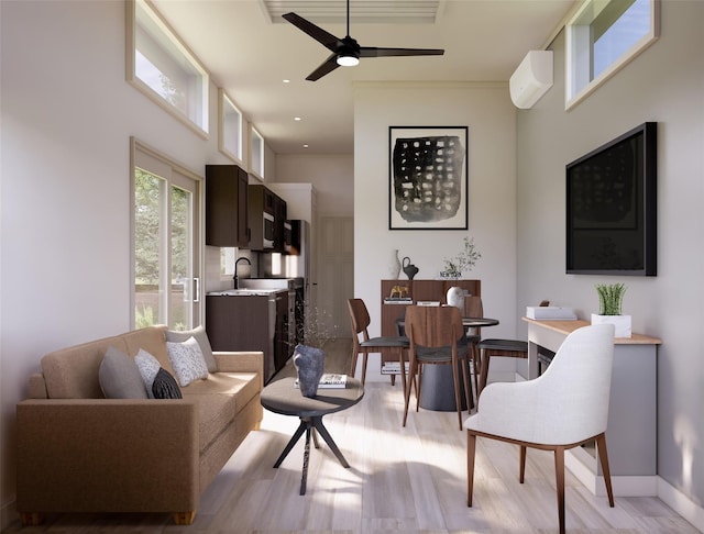 living room with sink, a wall mounted air conditioner, a towering ceiling, ceiling fan, and light hardwood / wood-style floors