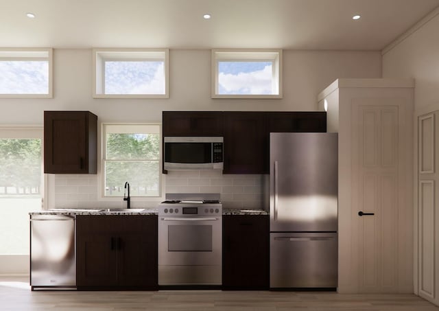 kitchen with appliances with stainless steel finishes, dark brown cabinets, light stone counters, decorative backsplash, and light wood-type flooring