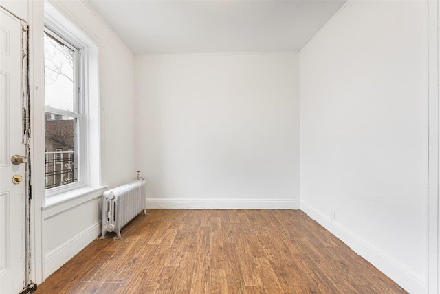 empty room with crown molding, radiator heating unit, and wood-type flooring