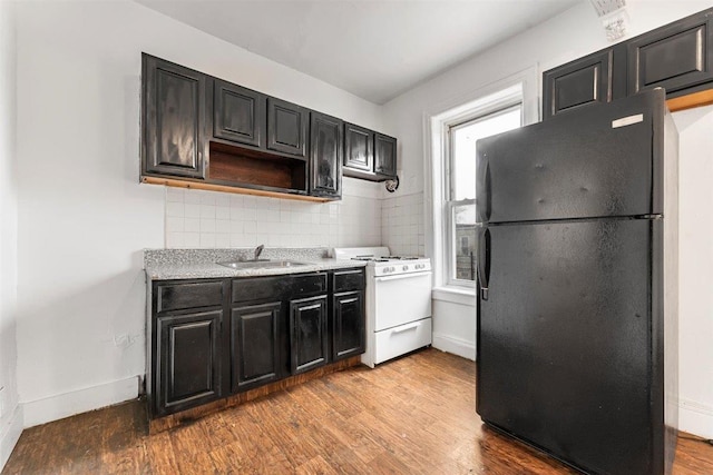 kitchen featuring black refrigerator, white gas range oven, light hardwood / wood-style flooring, sink, and tasteful backsplash