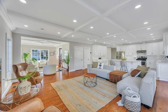 living room with coffered ceiling, beam ceiling, ornamental molding, and light hardwood / wood-style floors