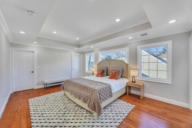 bedroom with ornamental molding, a tray ceiling, and light hardwood / wood-style flooring