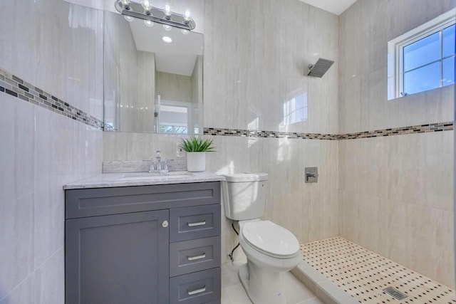 bathroom featuring vanity, tiled shower, tile walls, and toilet