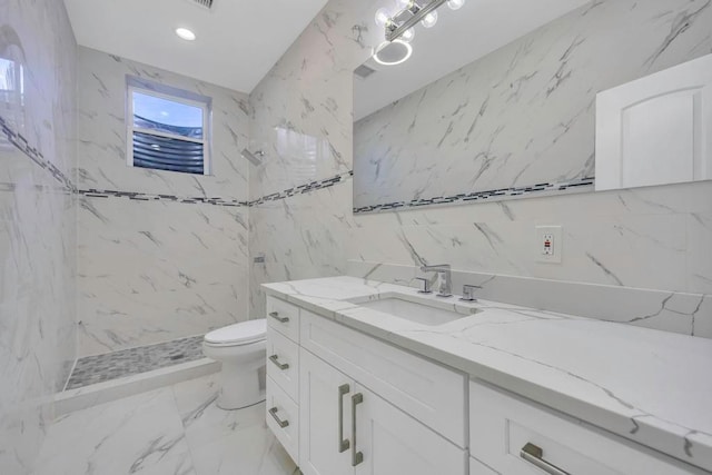 bathroom with a tile shower, vanity, tile walls, and toilet