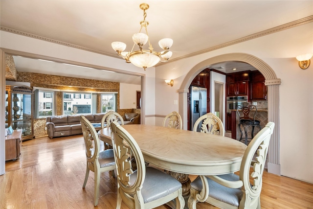 dining area with ornamental molding, light wood-type flooring, and an inviting chandelier