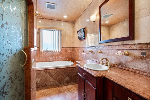 bathroom with vanity, tiled bath, a textured ceiling, and tile walls