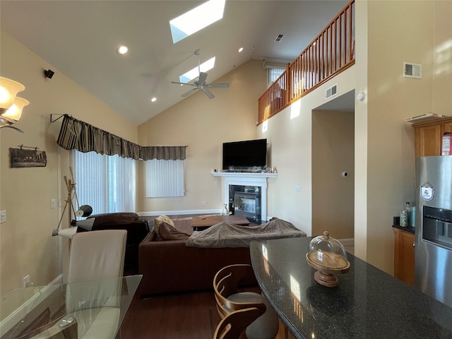 living room featuring ceiling fan, wood-type flooring, high vaulted ceiling, and a skylight