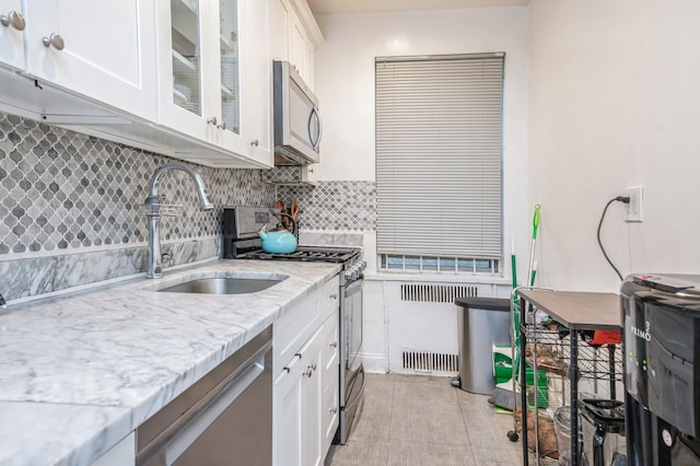 kitchen with appliances with stainless steel finishes, radiator, backsplash, sink, and white cabinetry