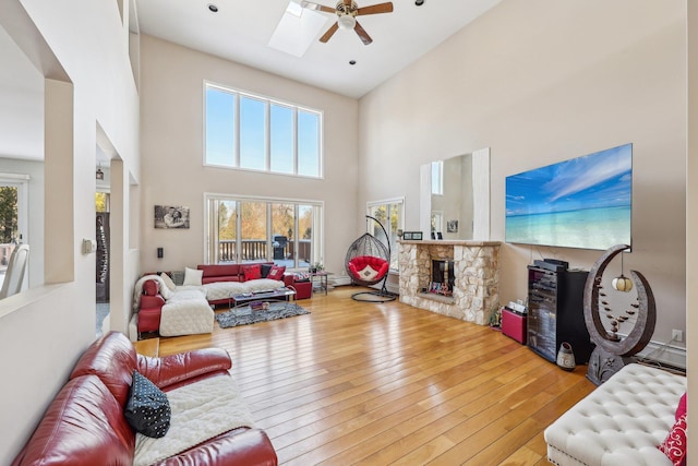 living room featuring a towering ceiling, a wealth of natural light, a fireplace, and light hardwood / wood-style flooring