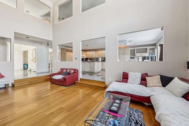 living room with ceiling fan, wood-type flooring, and a high ceiling