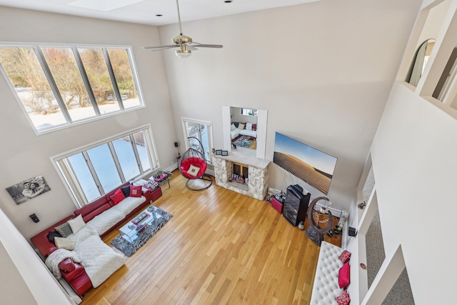 living room featuring ceiling fan, a towering ceiling, a skylight, and hardwood / wood-style floors