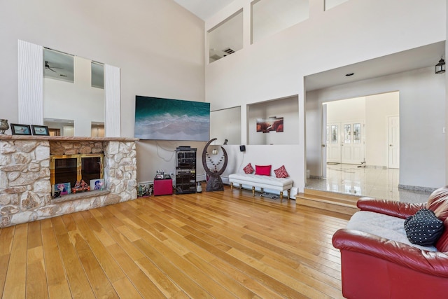 living room featuring hardwood / wood-style floors, a towering ceiling, and a stone fireplace