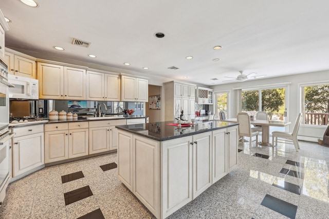 kitchen featuring a kitchen island, sink, dark stone countertops, white appliances, and cream cabinetry