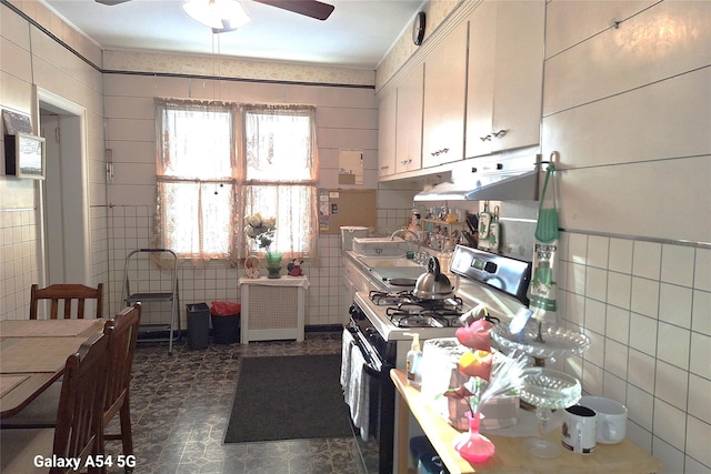 kitchen featuring radiator heating unit, tile walls, white cabinets, ceiling fan, and gas range