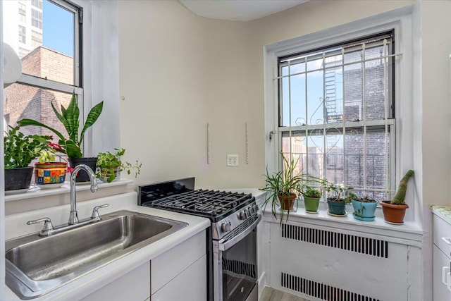 kitchen with white cabinets, sink, radiator heating unit, and stainless steel gas range