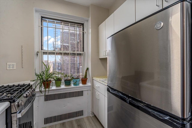 kitchen with radiator, light hardwood / wood-style floors, white cabinets, and appliances with stainless steel finishes