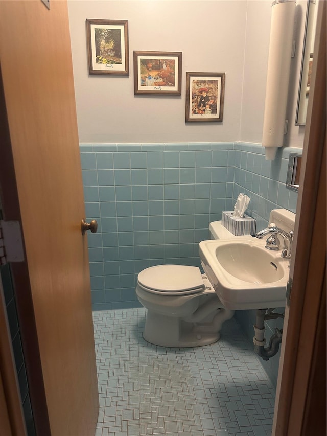 bathroom featuring toilet, sink, tile patterned flooring, and tile walls