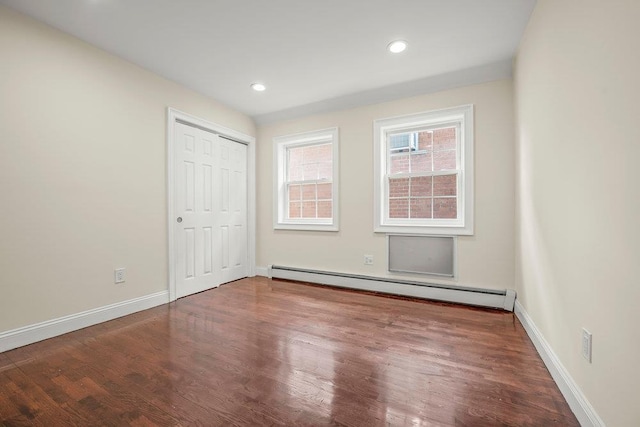 unfurnished bedroom with a baseboard heating unit and hardwood / wood-style flooring