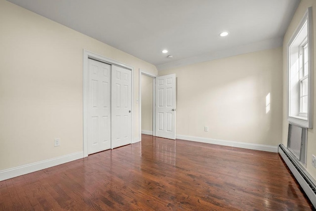 unfurnished bedroom featuring a baseboard radiator, dark hardwood / wood-style floors, and a closet