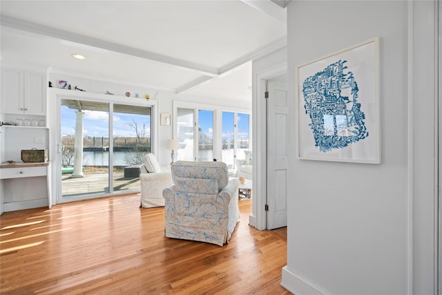 living area featuring beam ceiling, light hardwood / wood-style flooring, ornamental molding, and a water view