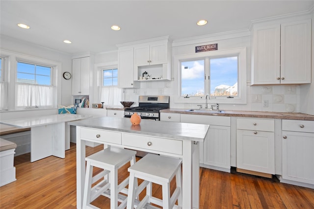 kitchen with sink, white cabinetry, dark hardwood / wood-style floors, stainless steel range with gas stovetop, and decorative backsplash