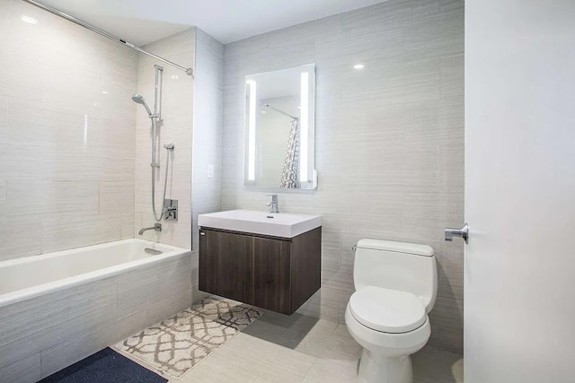 full bathroom with tiled shower / bath, tile walls, tile patterned flooring, vanity, and toilet