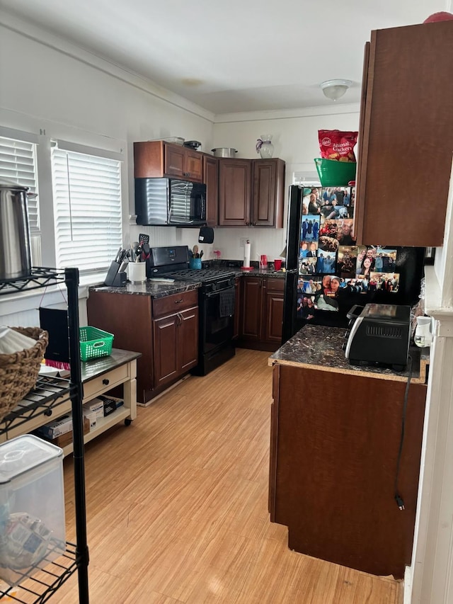 kitchen with dark brown cabinetry, crown molding, black appliances, and light wood-type flooring